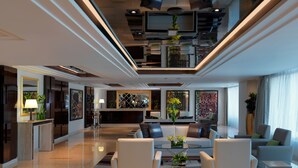 Un hall d’hôtel moderne comprenant un comptoir d’accueil, un espace salon et un escalier menant à un étage supérieur.