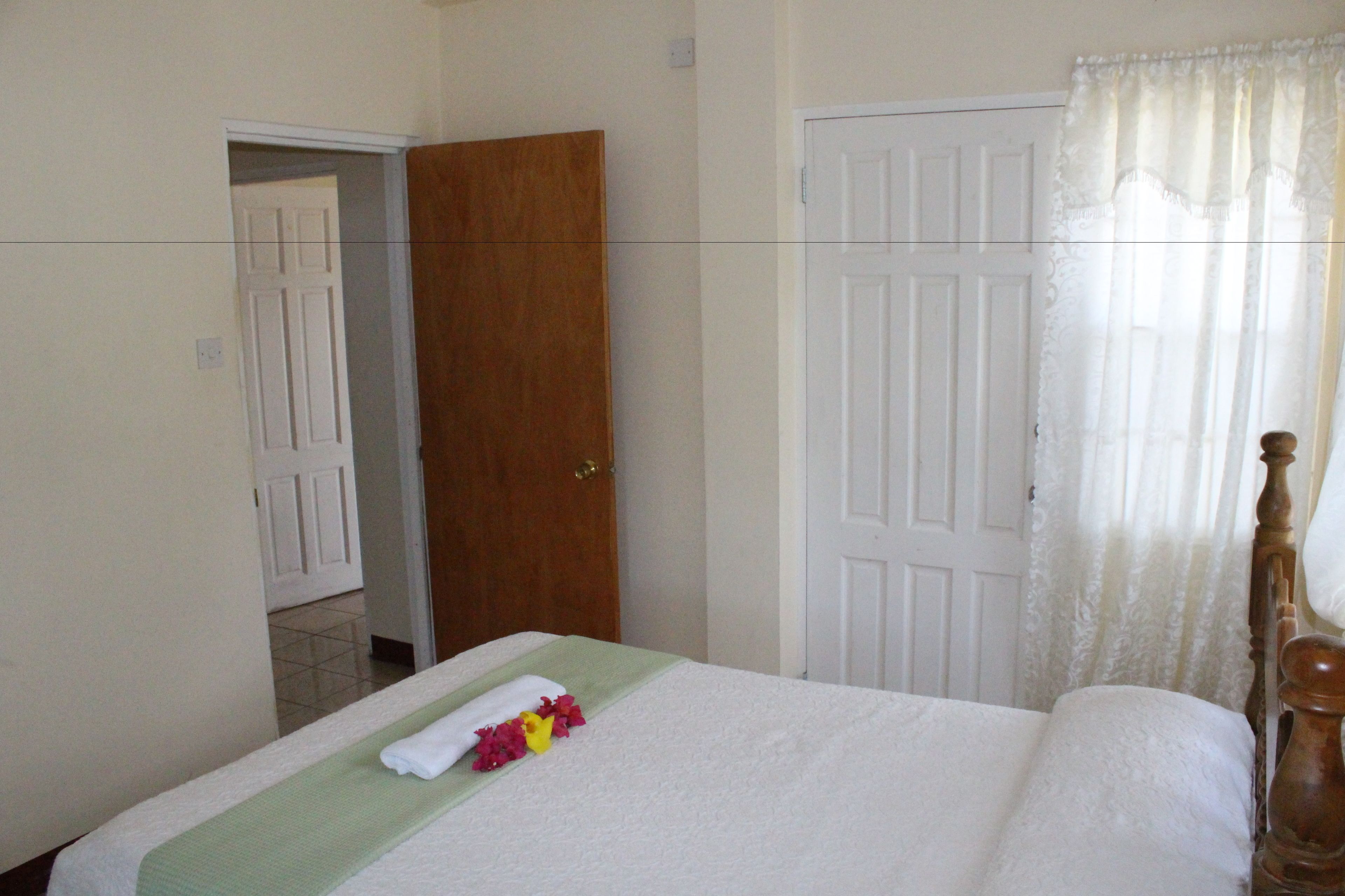 A hotel room with a bed, a wooden door, and a white curtain.