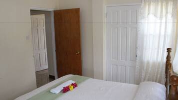 A hotel room with a bed, a wooden door, and a white curtain.
