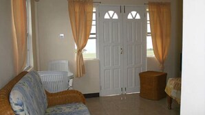 A room with a wicker sofa, a small table, and a white door with windows. - Relax Inn Grenada West Indies (St. George's)