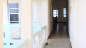 A corridor with a tiled floor, white walls, and a balcony with a white railing. - Relax Inn Grenada West Indies (St. George's)