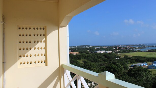 A balcony with a view of a coastal town, a drainage grate, and a railing. - Relax Inn Grenada West Indies (St. George's)
