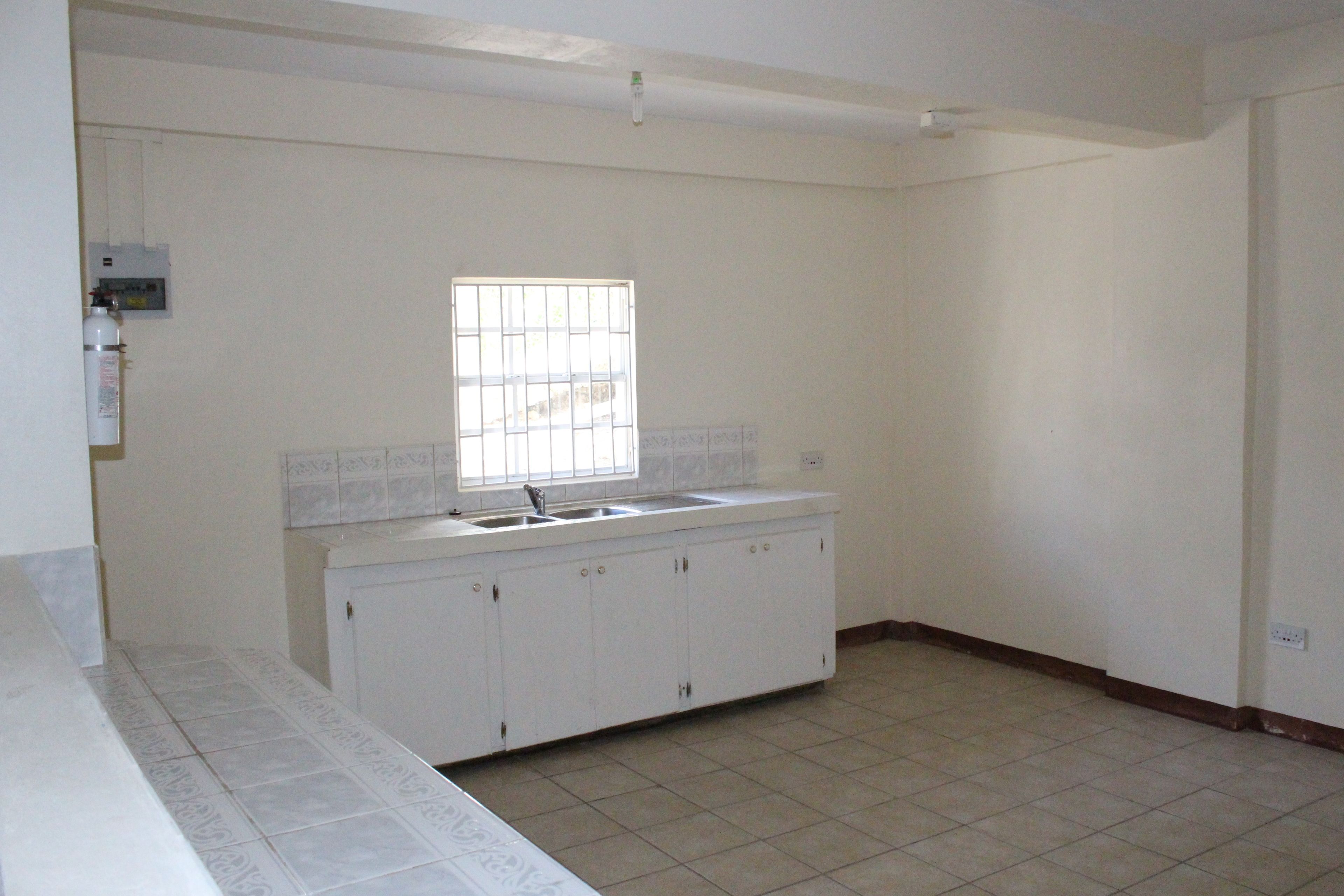Una cocina con armarios blancos, una ventana con rejas y piso de baldosas.
