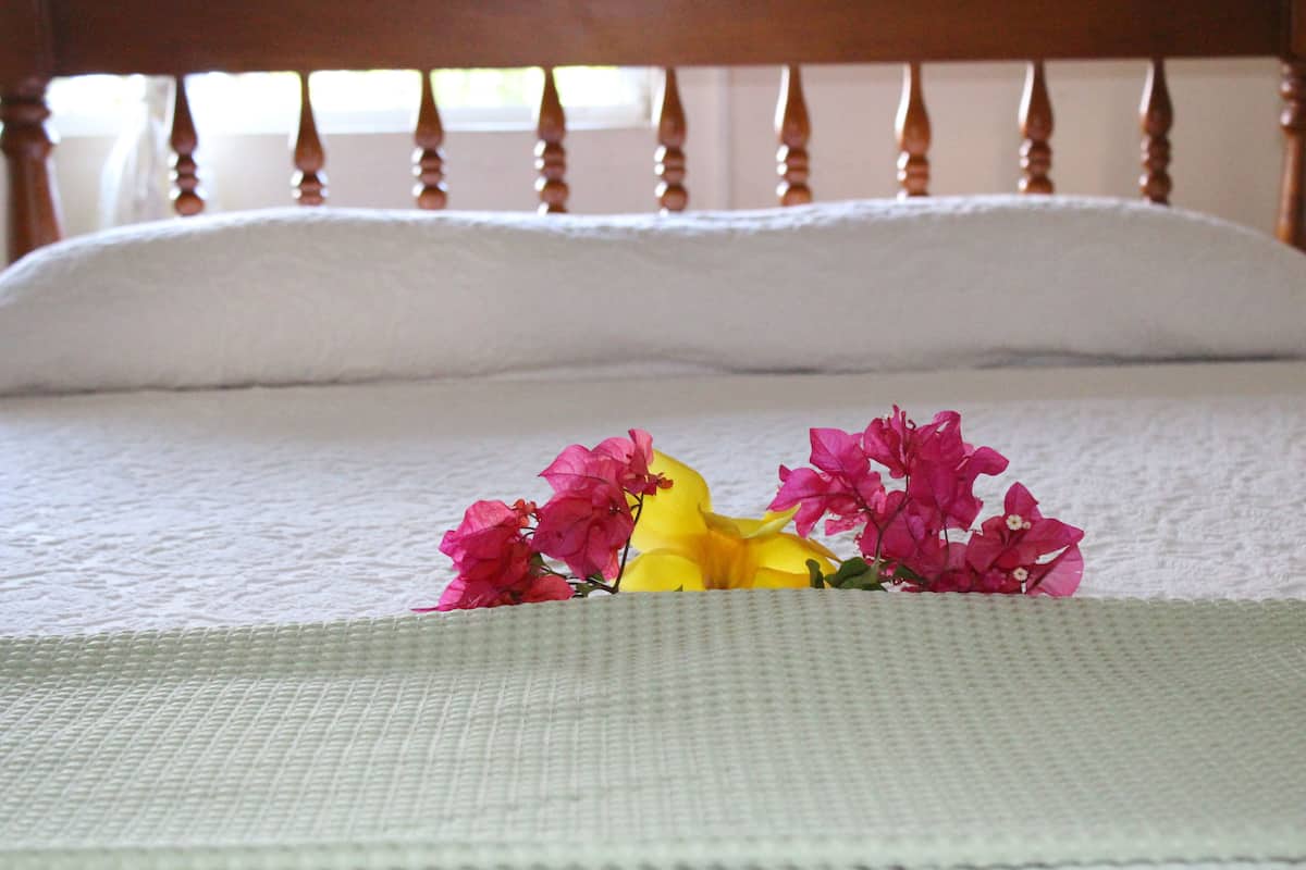 A bed with a white sheet and a green blanket, and pink and yellow flowers on the bed.