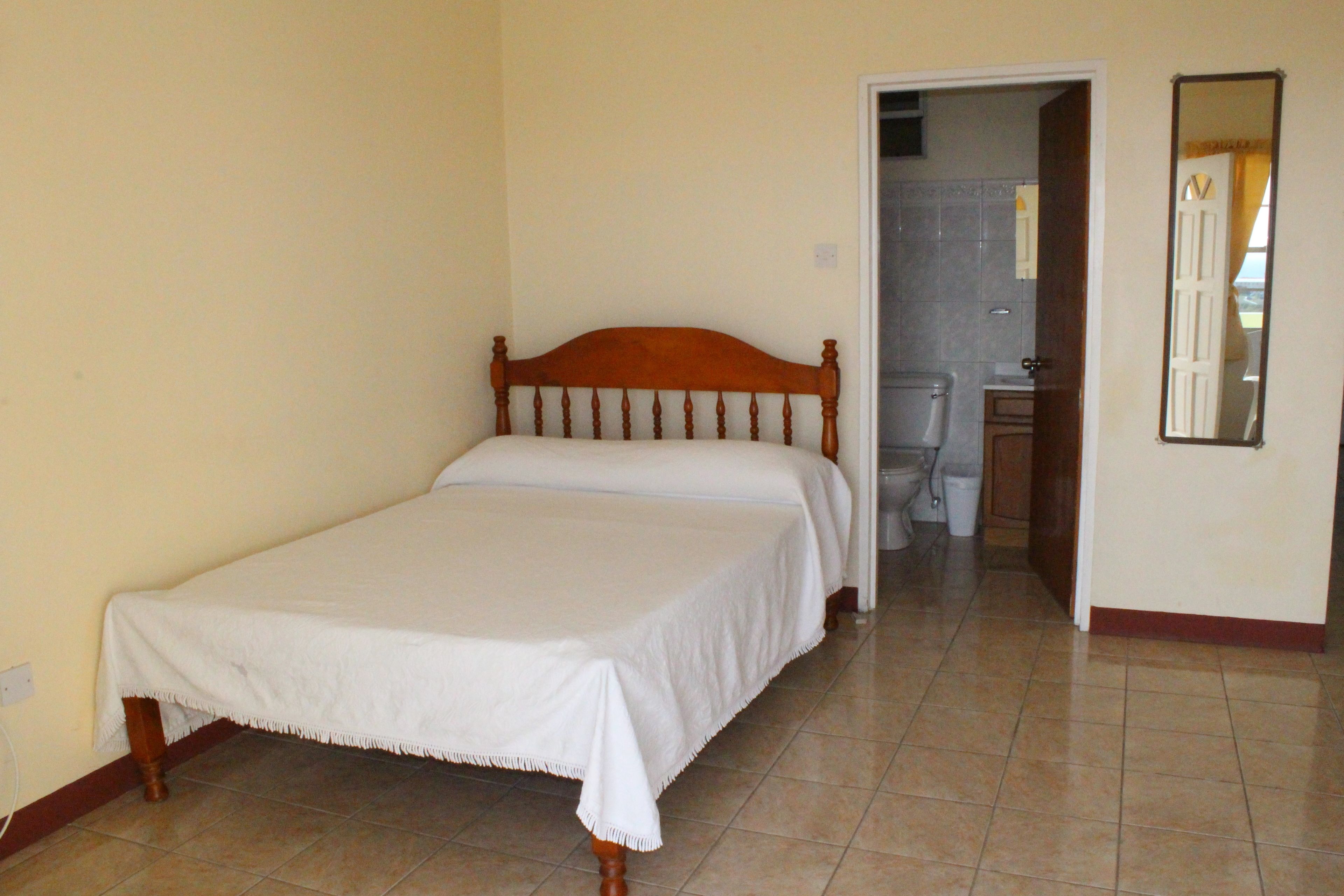 A bedroom with a single bed, a bathroom with a toilet and sink, and a mirror on the wall.