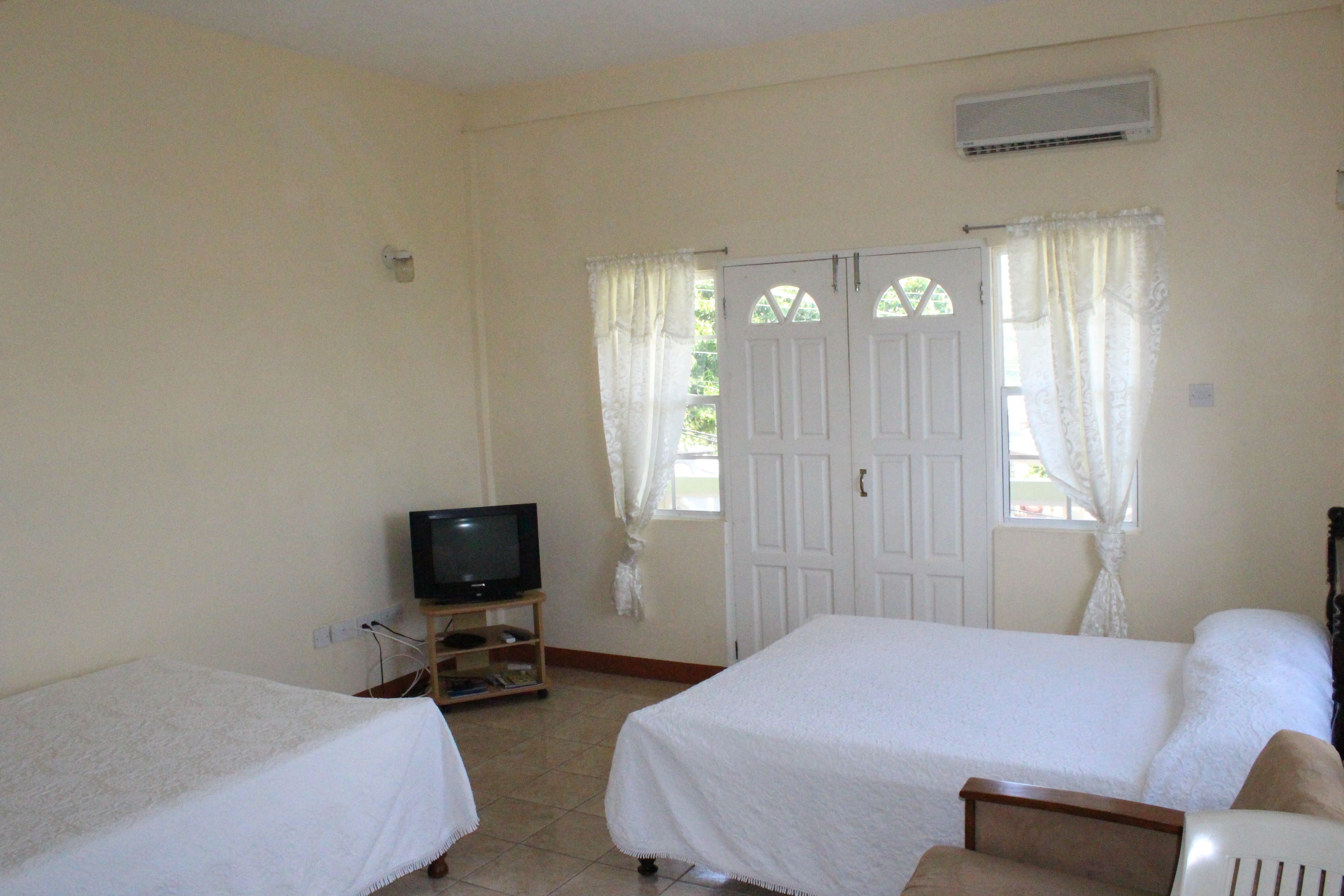 Una habitación con dos camas, un televisor sobre un mueble y una puerta con cortinas.