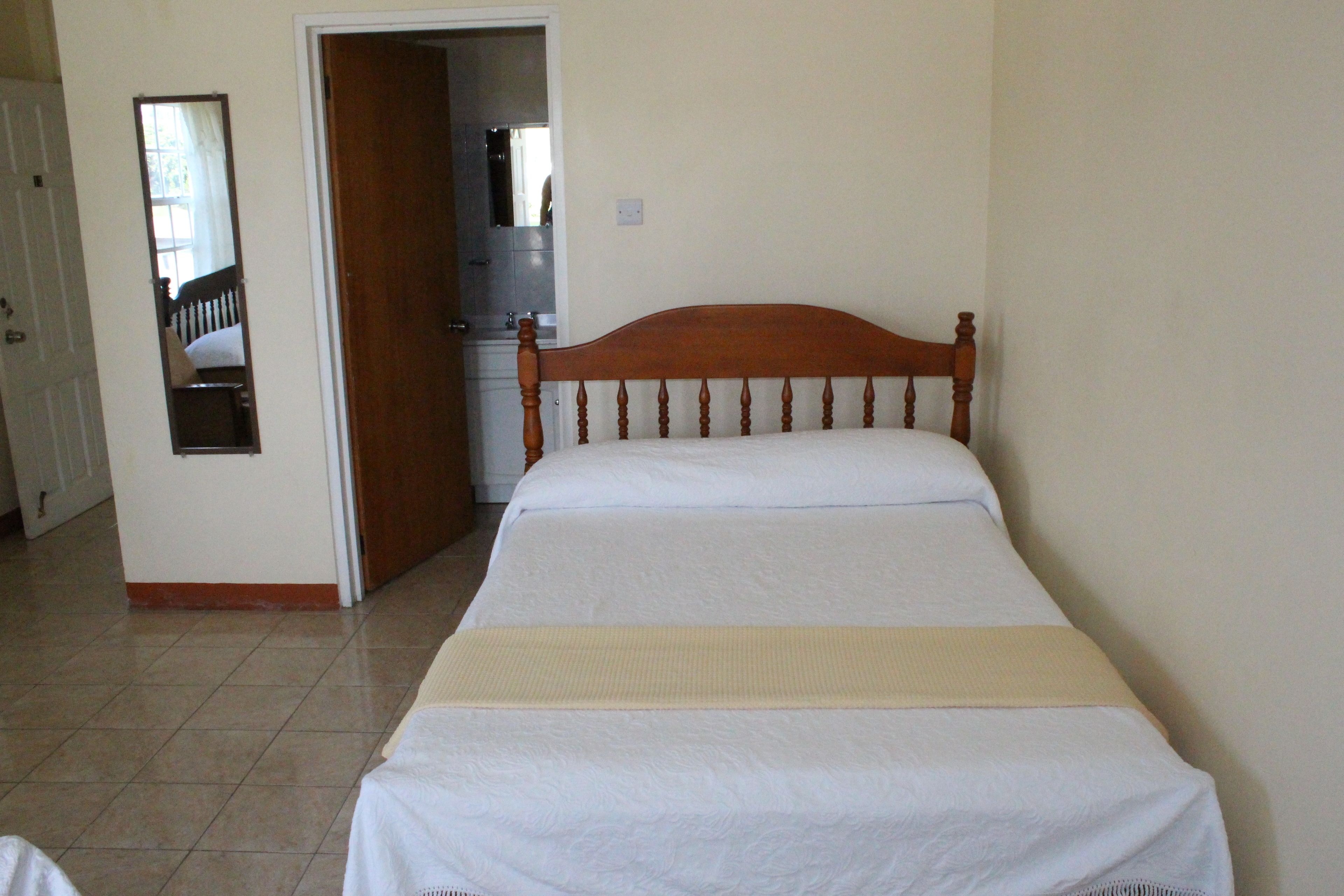 A bedroom with a wooden bed, a mirror, and a door leading to a bathroom.