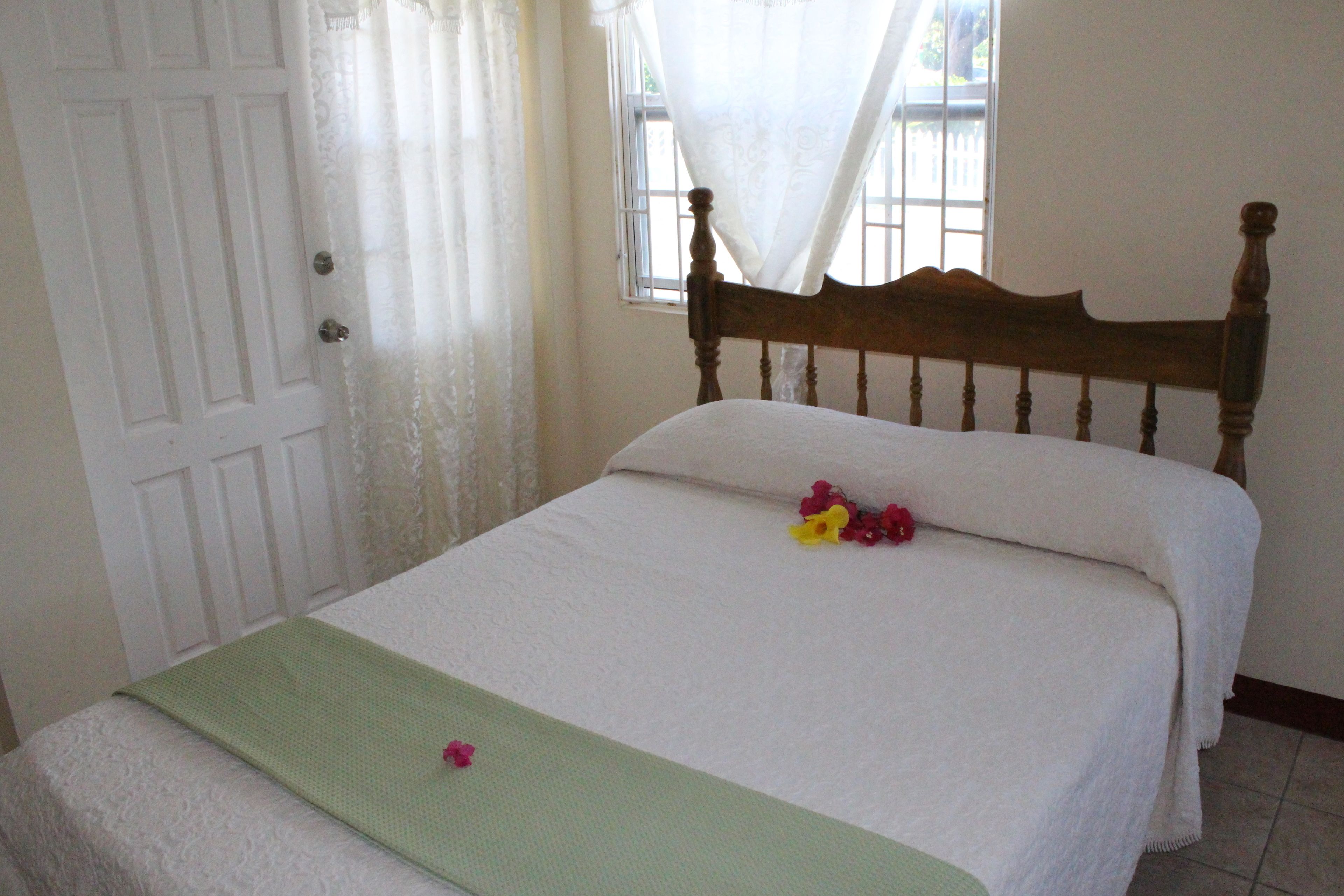 Uma cama bem arrumada com um edredom verde, uma almofada branca e uma única flor.