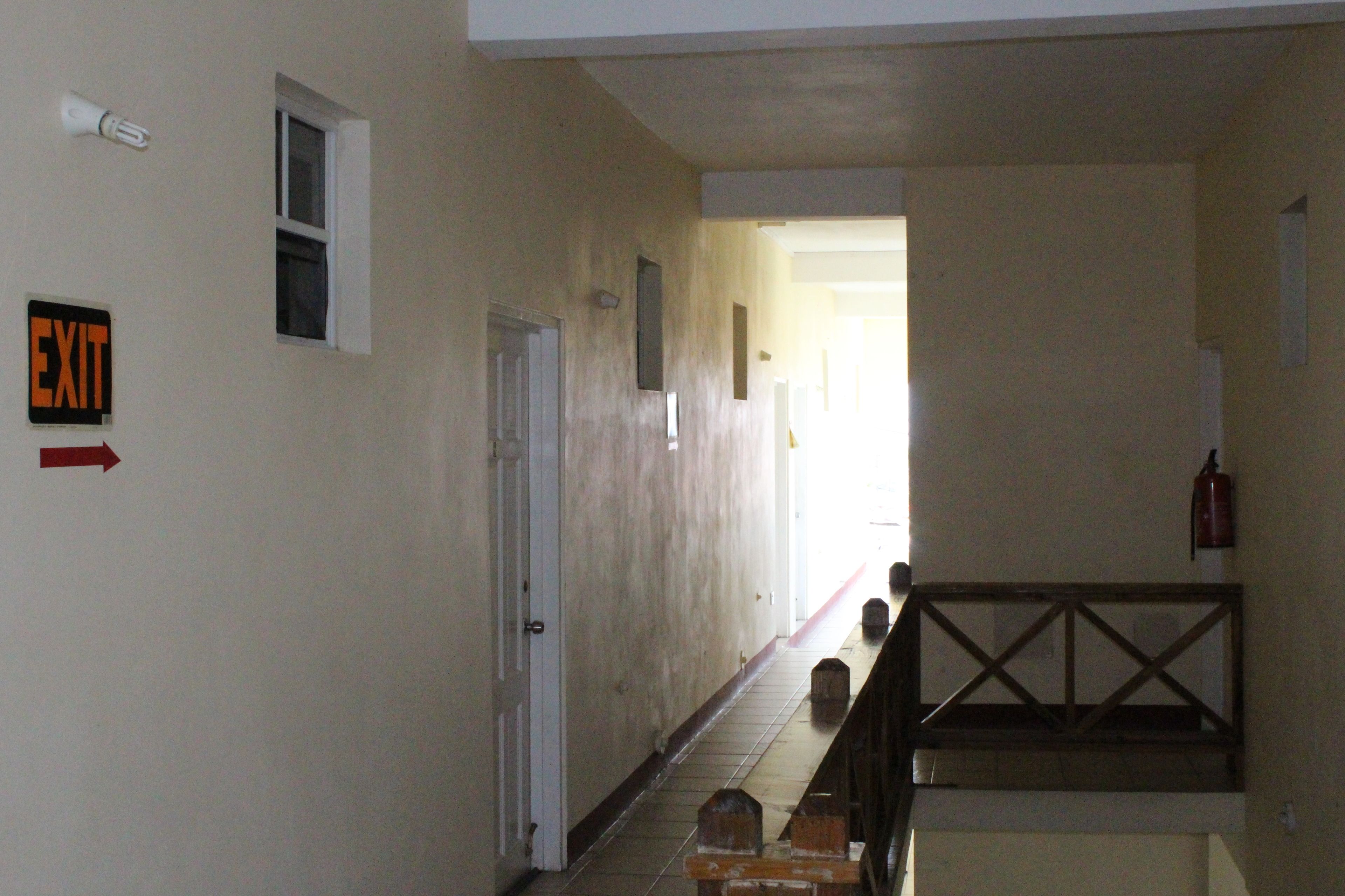 A hallway with an exit sign, a door, and a staircase with a railing.