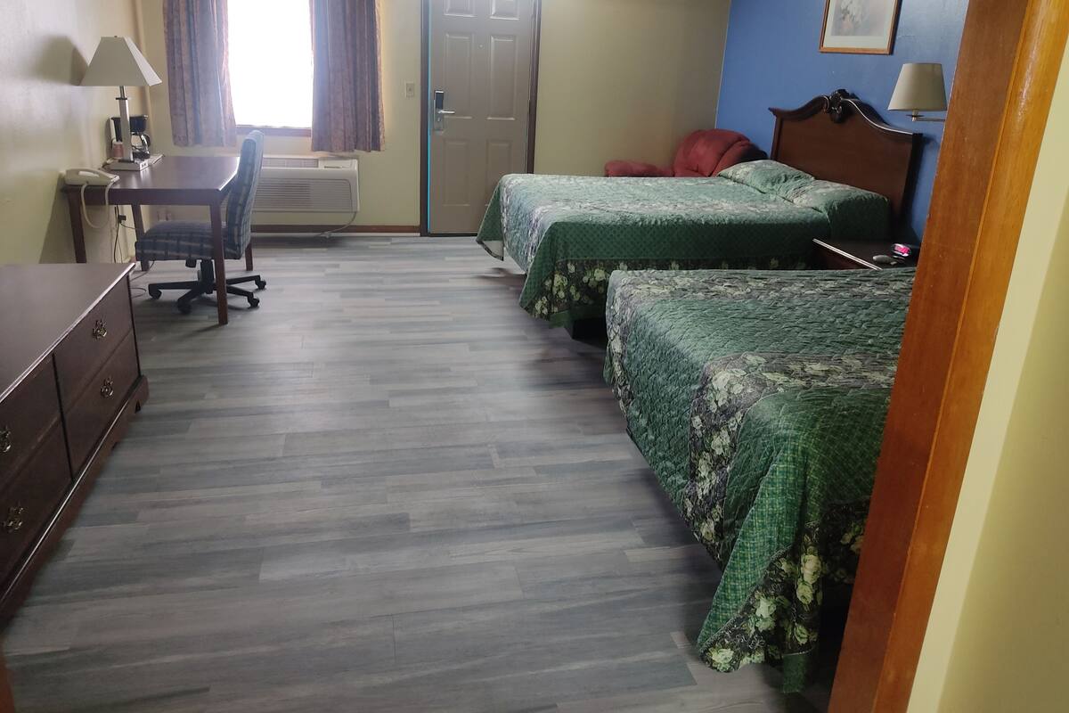 Quarto de hotel com duas camas, uma escrivaninha, uma cadeira e um guarda-roupa.