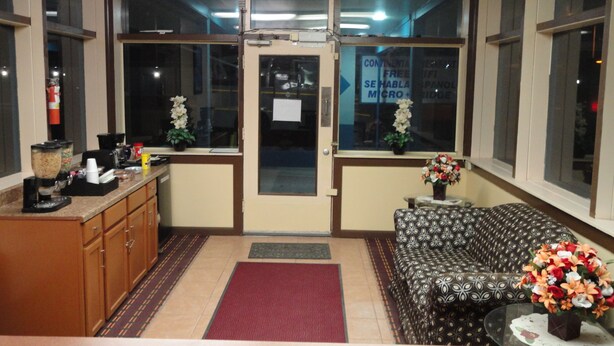 A reception area with a sofa, a coffee station, a flower arrangement, and a door with a sign.
