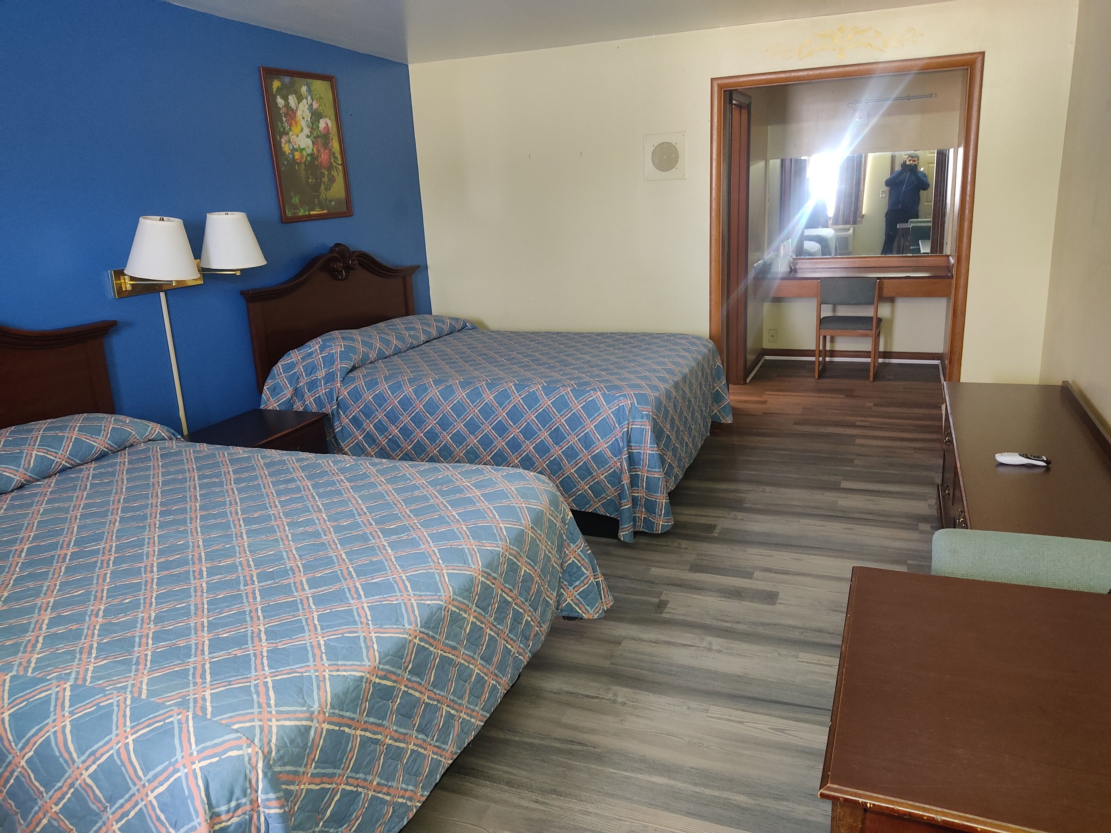 A hotel room with two beds, a desk, a chair, and a mirror.