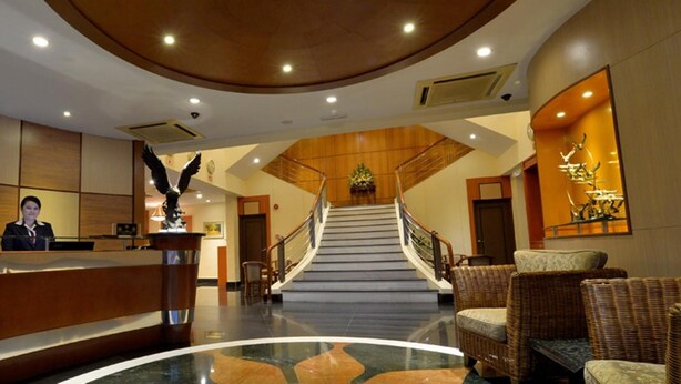 A hotel lobby with a reception desk, a staircase, and wicker furniture. - Asiana Hotel (Kota Kinabalu)