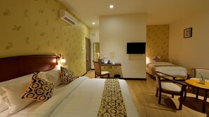 A hotel room with a large bed, two smaller beds, a desk with a chair, a television, and a small table with a plant. - Asiana Hotel (Kota Kinabalu)