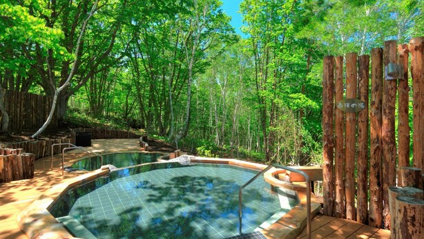 Un jacuzzi rodeado por una terraza de madera y un área boscosa.