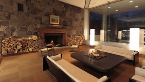 Una sala moderna con pared de piedra, chimenea y un ventanal con vista a un paisaje urbano.