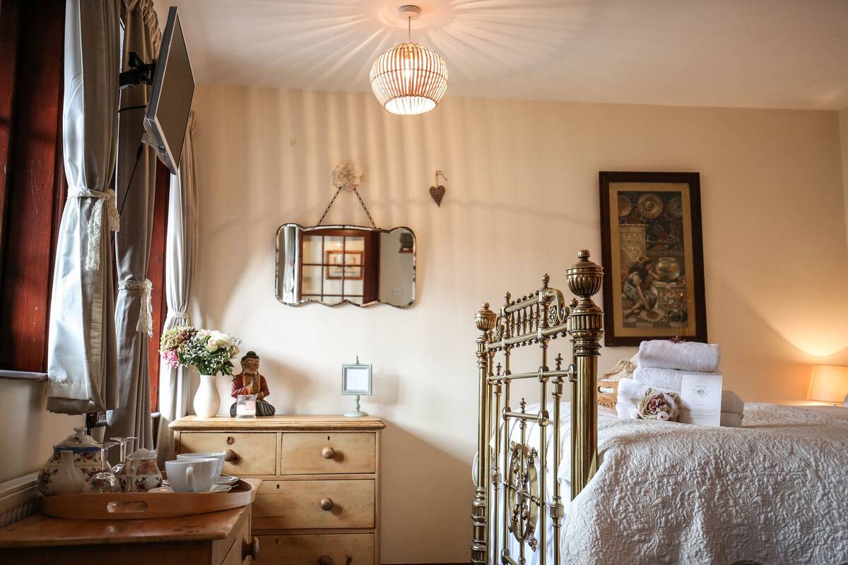 A bedroom with a bed, a dresser, a mirror, a hanging light fixture, and a framed picture on the wall.