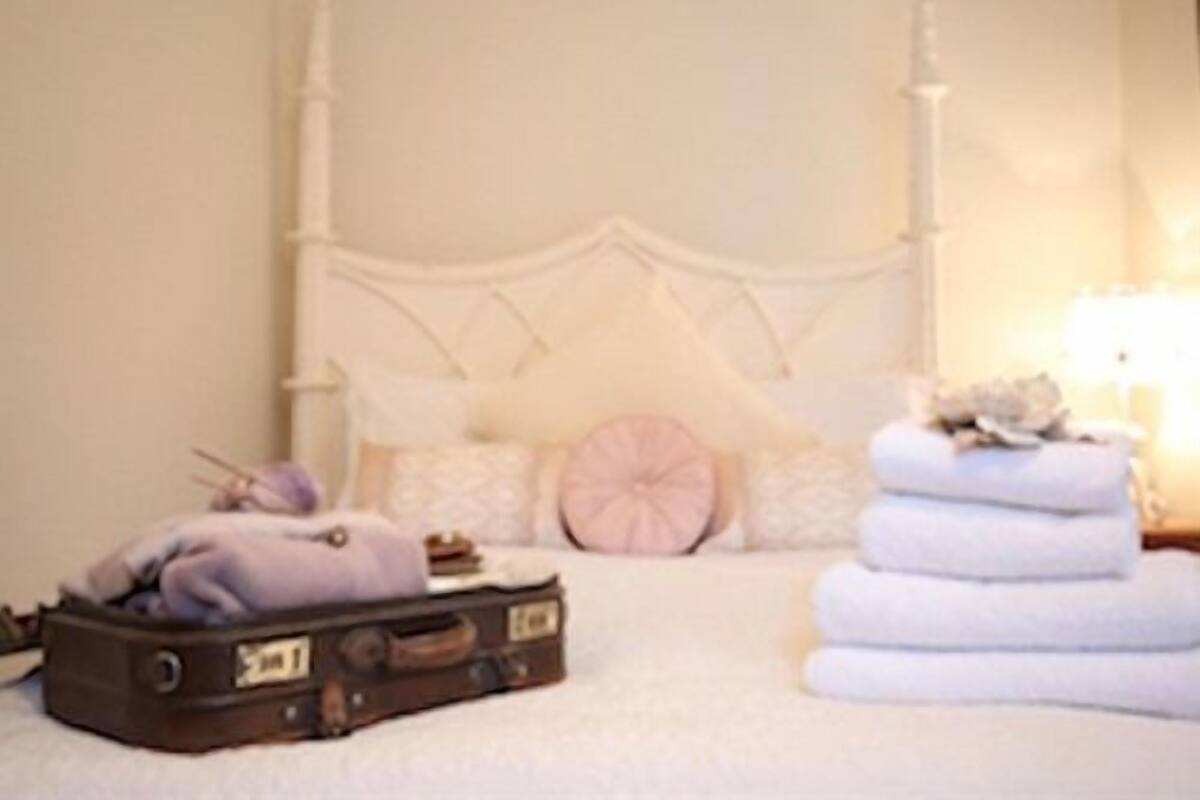 A neatly made bed with a white headboard, a suitcase, and a stack of folded towels.