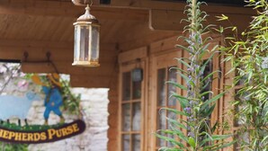 A rustic wooden building with a hanging lantern, a sign reading "Shepherds Purse," and various potted plants.