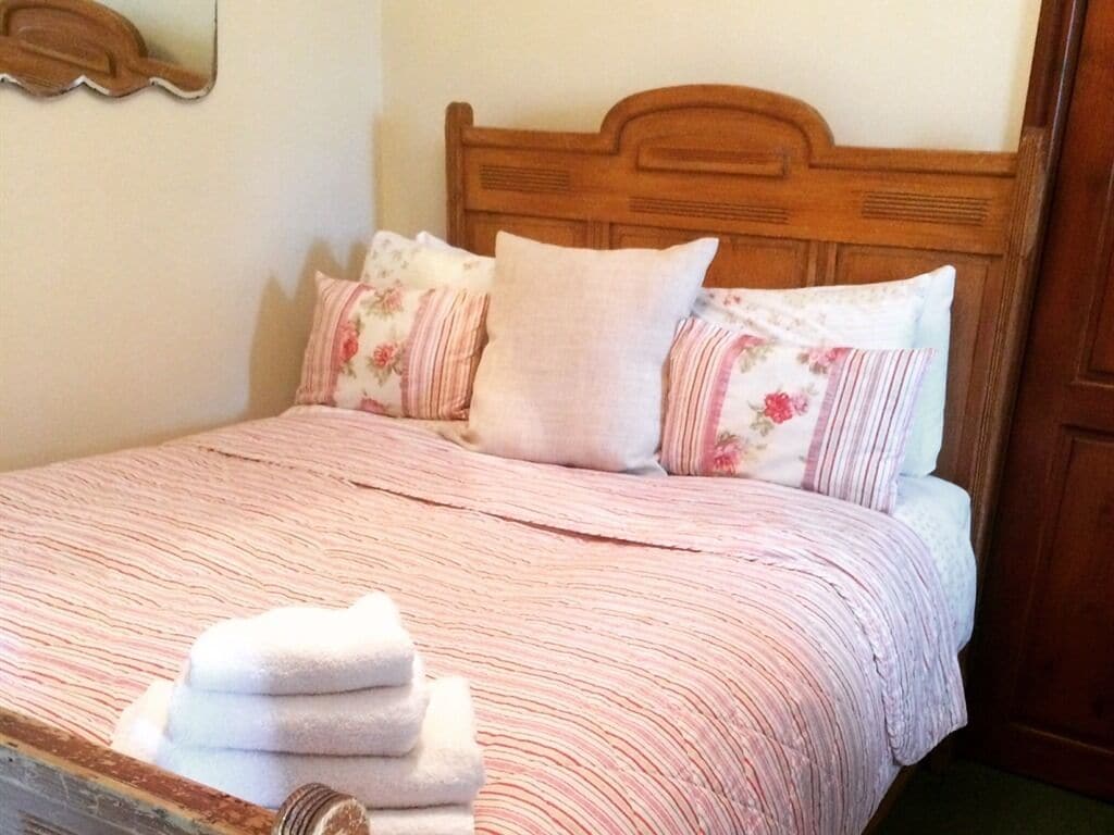 Een net opgemaakt bed met een gestreept dekbedovertrek, twee kussens met bloemmotieven, en een stapel opgevouwen handdoeken.