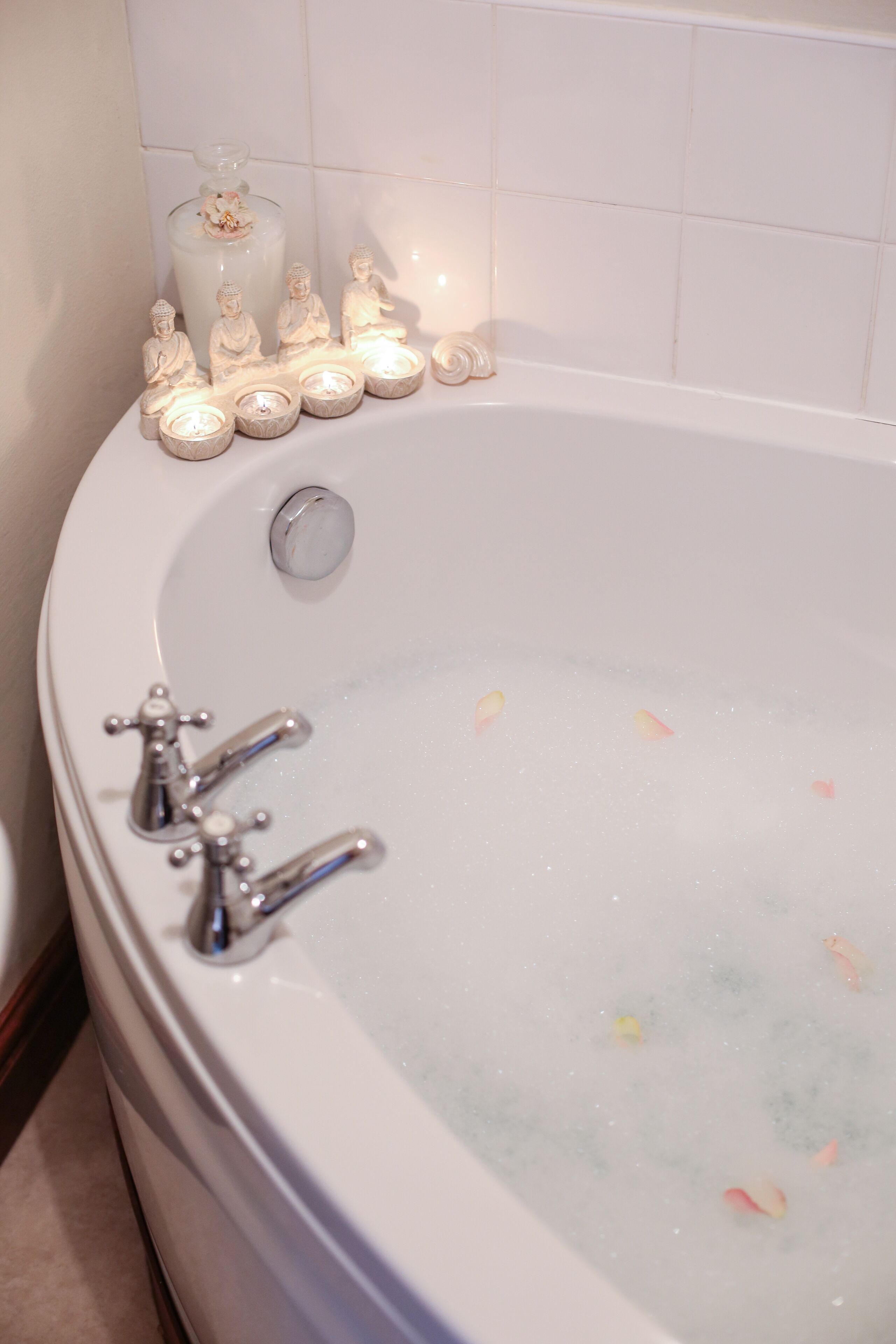Une baignoire dotée de plusieurs robinets, un récipient en verre contenant une fleur et plusieurs bougies allumées.
