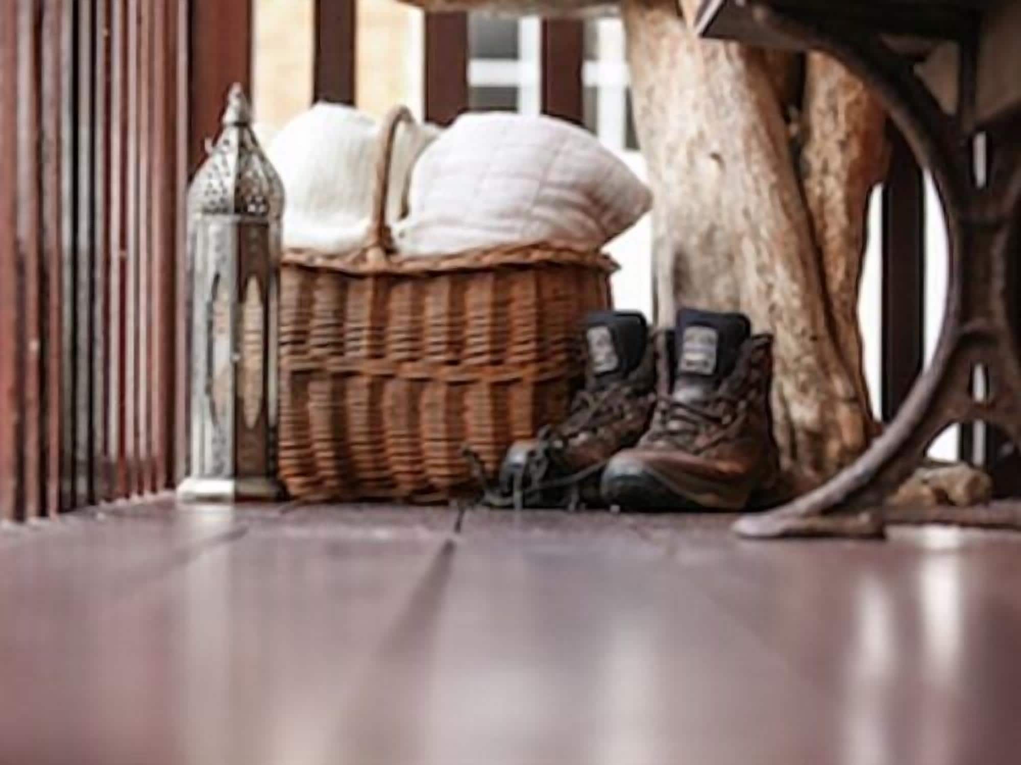 Un plancher en bois, avec un panier en osier contenant des coussins et une paire de bottes.