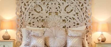 A bedroom with a decorative headboard, two bedside tables with lamps, and a bedside table with a tray.