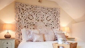 A bedroom with a decorative headboard, a bed with multiple pillows, two bedside tables with lamps, and a wooden chest of drawers.
