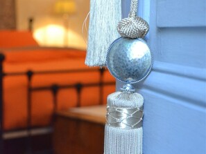 A close-up of a decorative silver ornament with a tassel, hanging on a door. - Le Petit Chou (Entraygues-sur-Truyere)