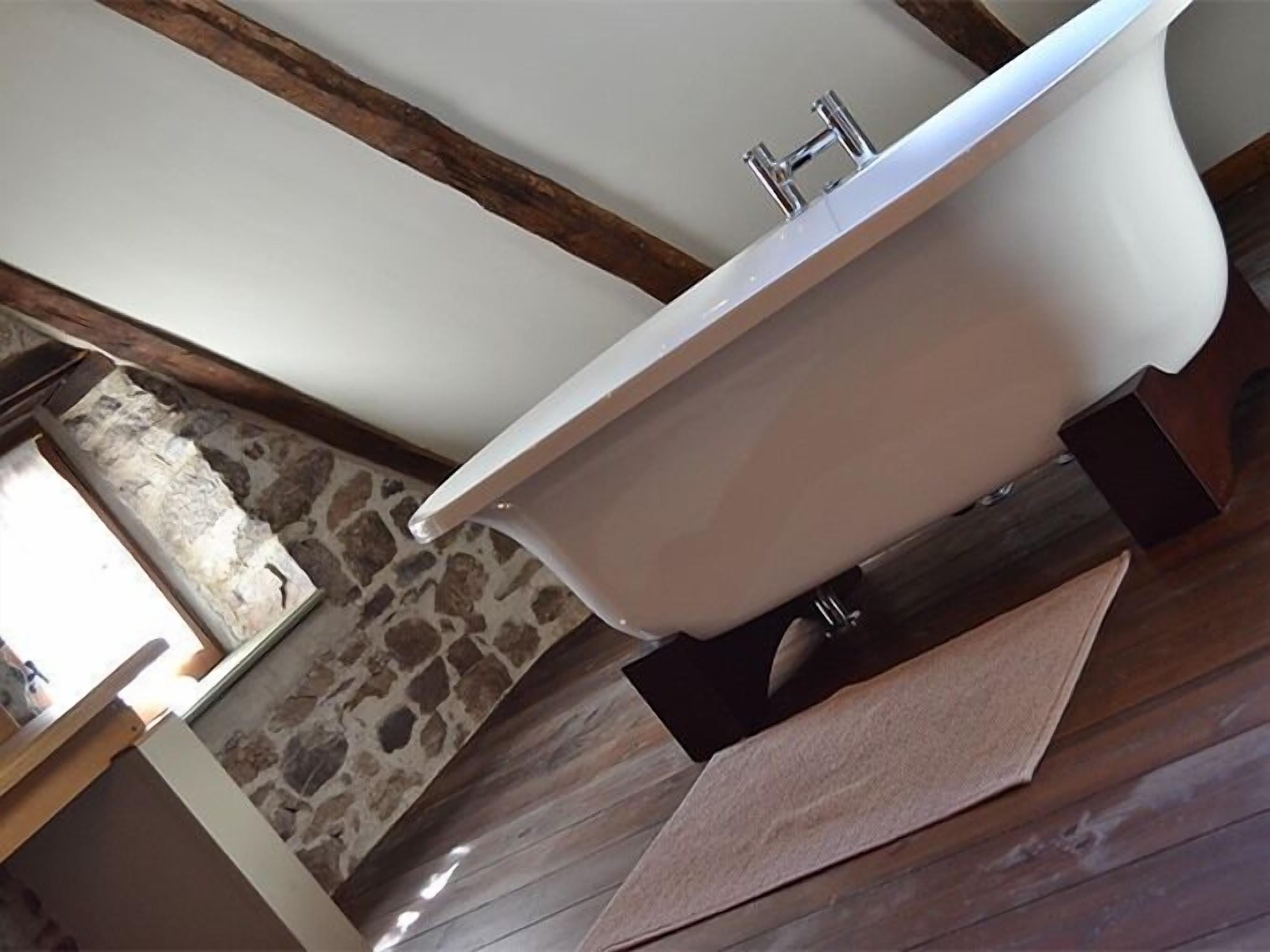Ein modernes Badezimmer mit freitstehender Badewanne, Steinwand und Holzboden.