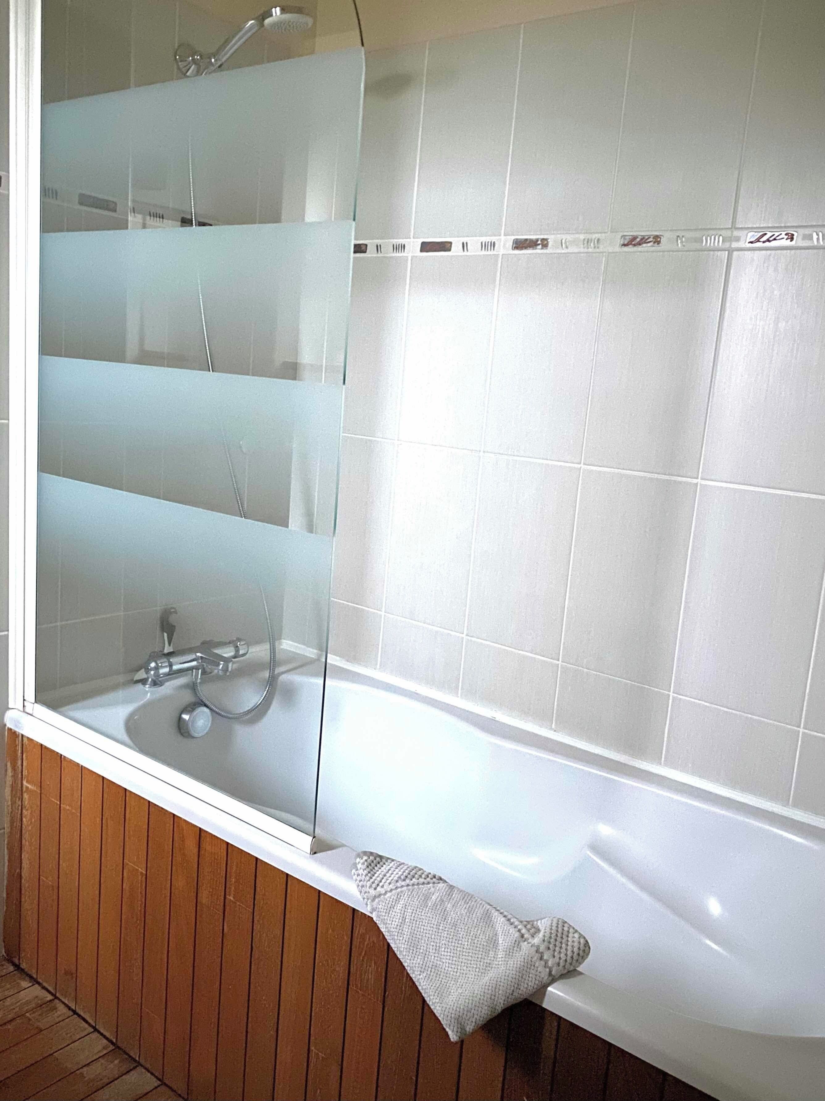 A modern bathroom with a glass shower enclosure, a white bathtub, and wooden paneling.