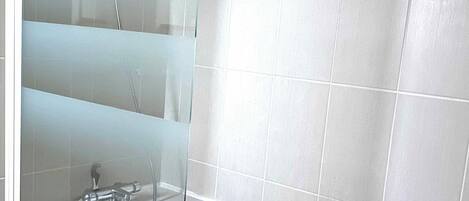 A modern bathroom with a glass shower enclosure, a white bathtub, and wooden paneling.