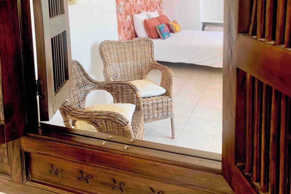 Une pièce comprenant un lit, deux fauteuils en osier, un luminaire suspendu et un cadre de miroir décoratif.