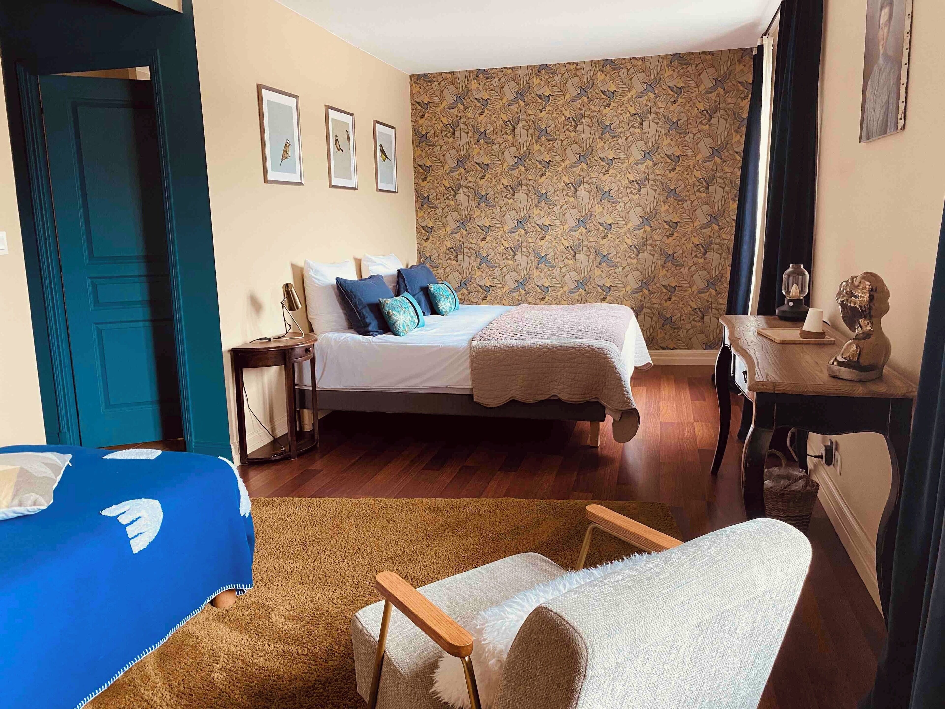 A bedroom with a bed, bedside tables, a chair, a dresser, and a patterned wallpaper.