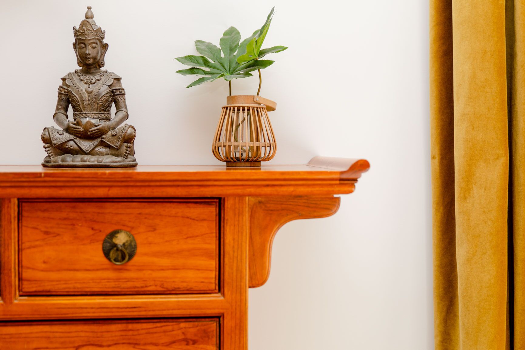 A wooden cabinet with a Buddha statue and a potted plant on top.