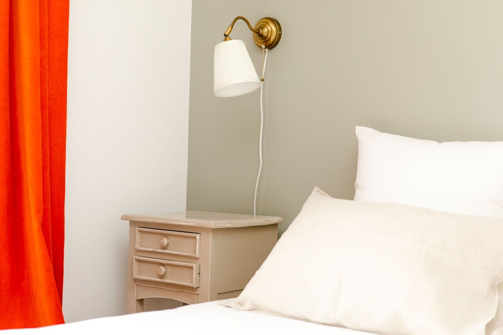 A bedroom with a bed, a nightstand, a lamp, and a curtain.
