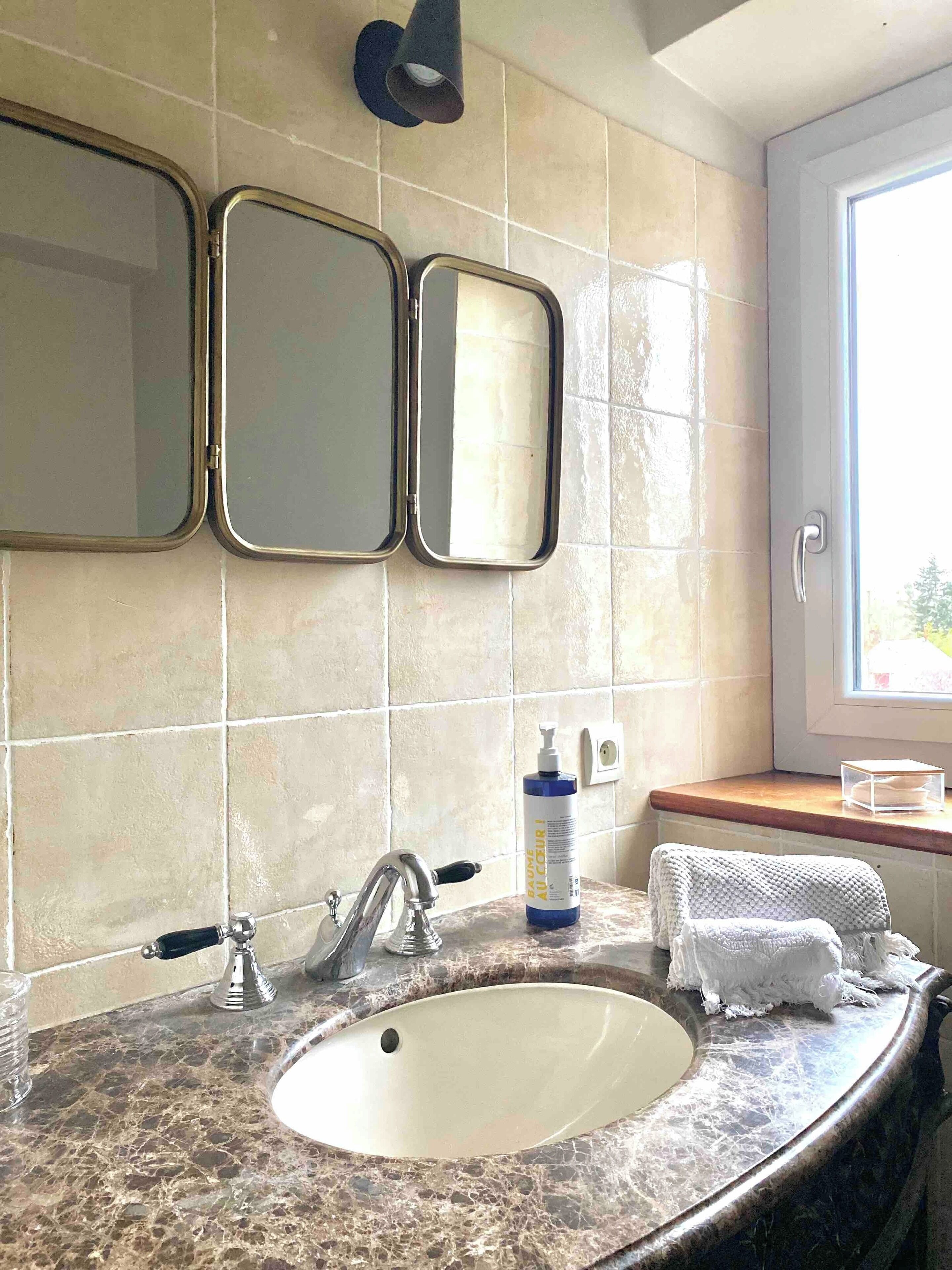 A bathroom with a marble sink, two wall-mounted mirrors, a towel rack, and a window with a view.