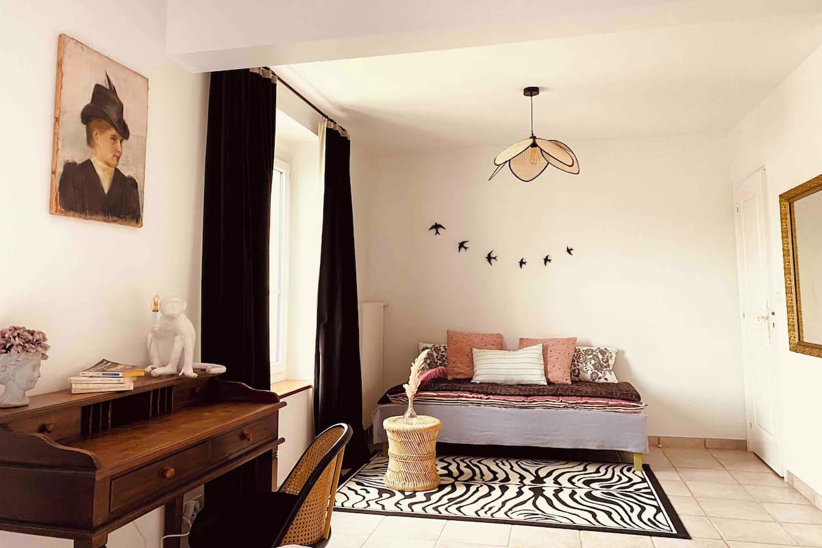 Une chambre avec un lit, un bureau, une chaise, un tapis à motifs zébrés, un luminaire suspendu et un tableau accroché au mur.