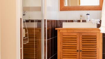 A bathroom with a glass shower enclosure, a wooden vanity with a mirror, and dark tiled flooring.