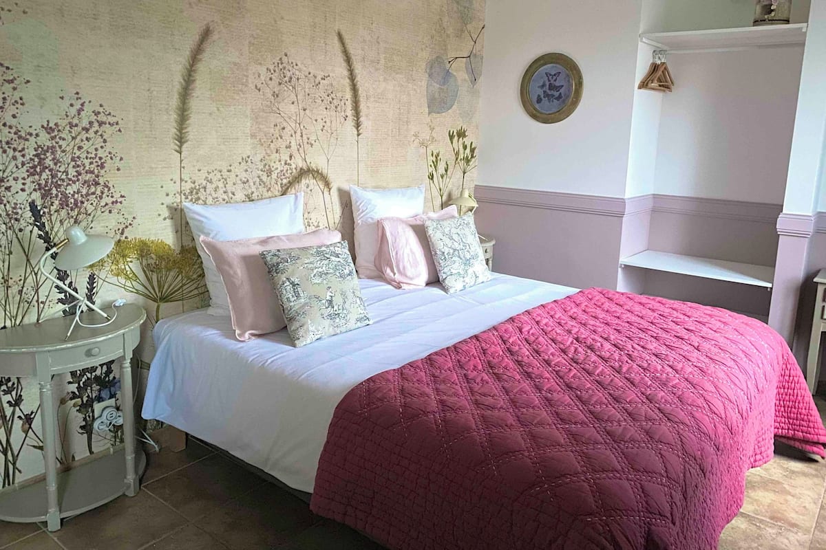 Une chambre à coucher bien rangée, avec un grand lit, une table de chevet avec une lampe et une étagère murale agrémentée d  ’objets décoratifs.
