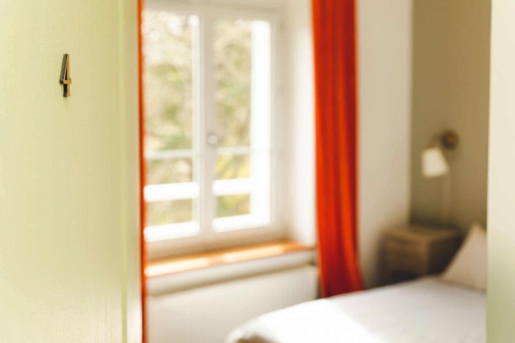 Una habitación con una cama, una ventana con cortinas rojas y una mesita de noche con una lámpara.