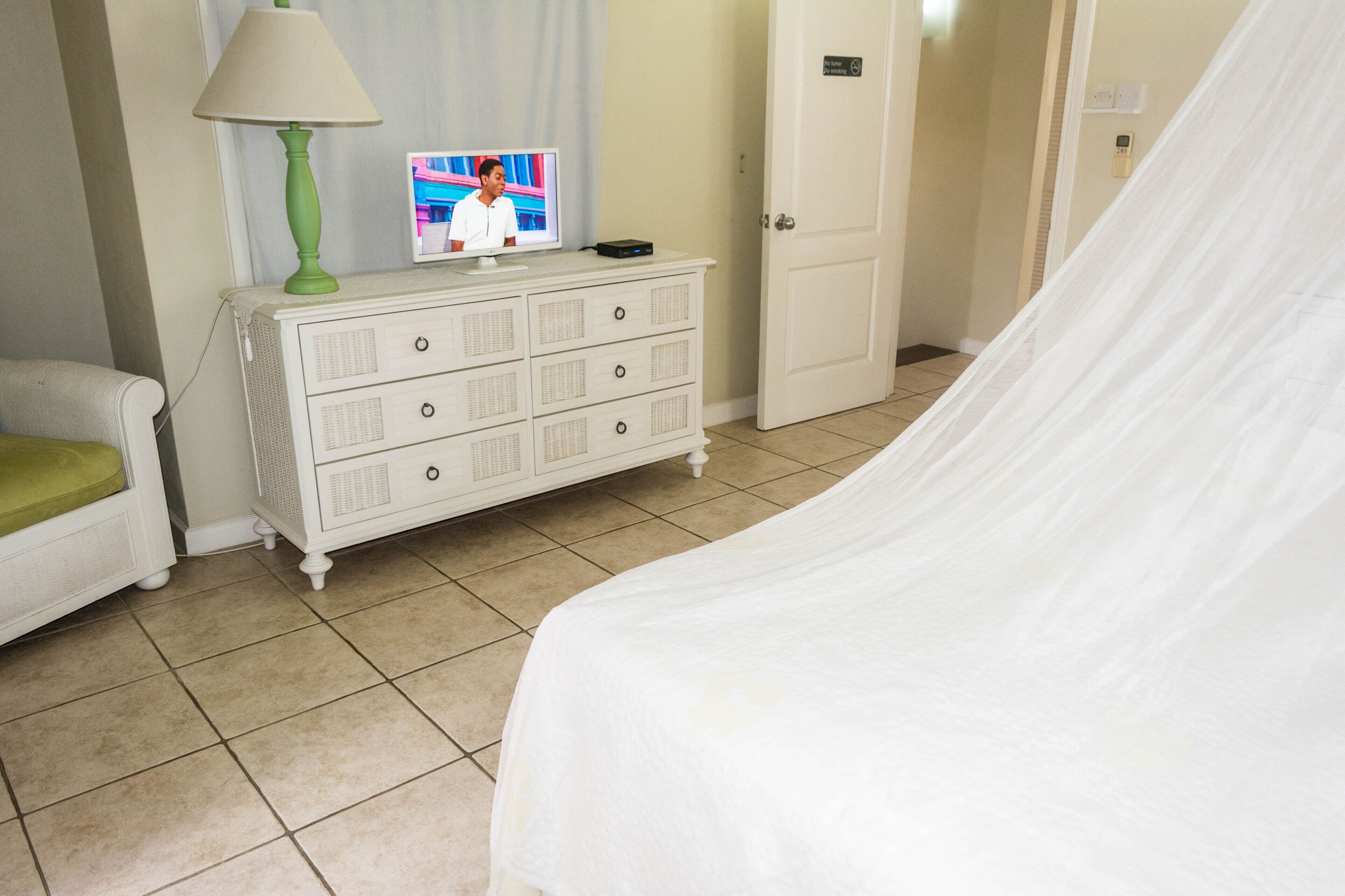 Une chambre d’hôtel avec un lit, une commode blanche sur laquelle se trouve une lampe verte, et un téléviseur posé sur la commode.
