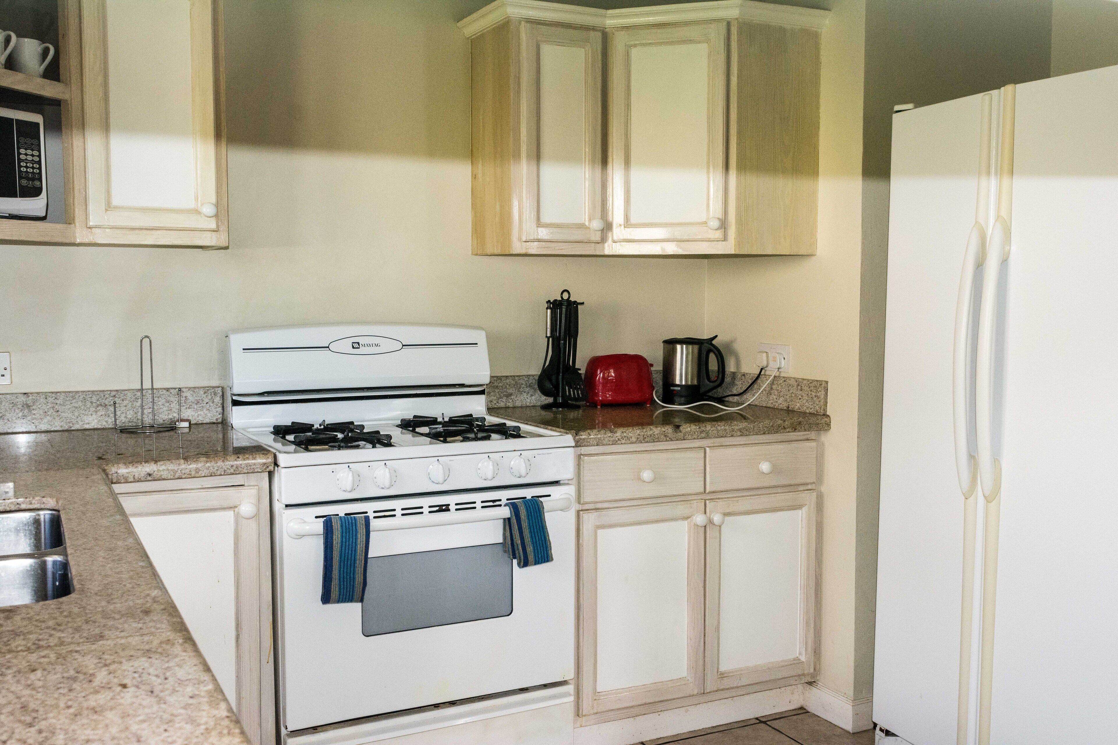 A kitchen with a white stove, wooden cabinets, a red coffee maker, and a white refrigerator.