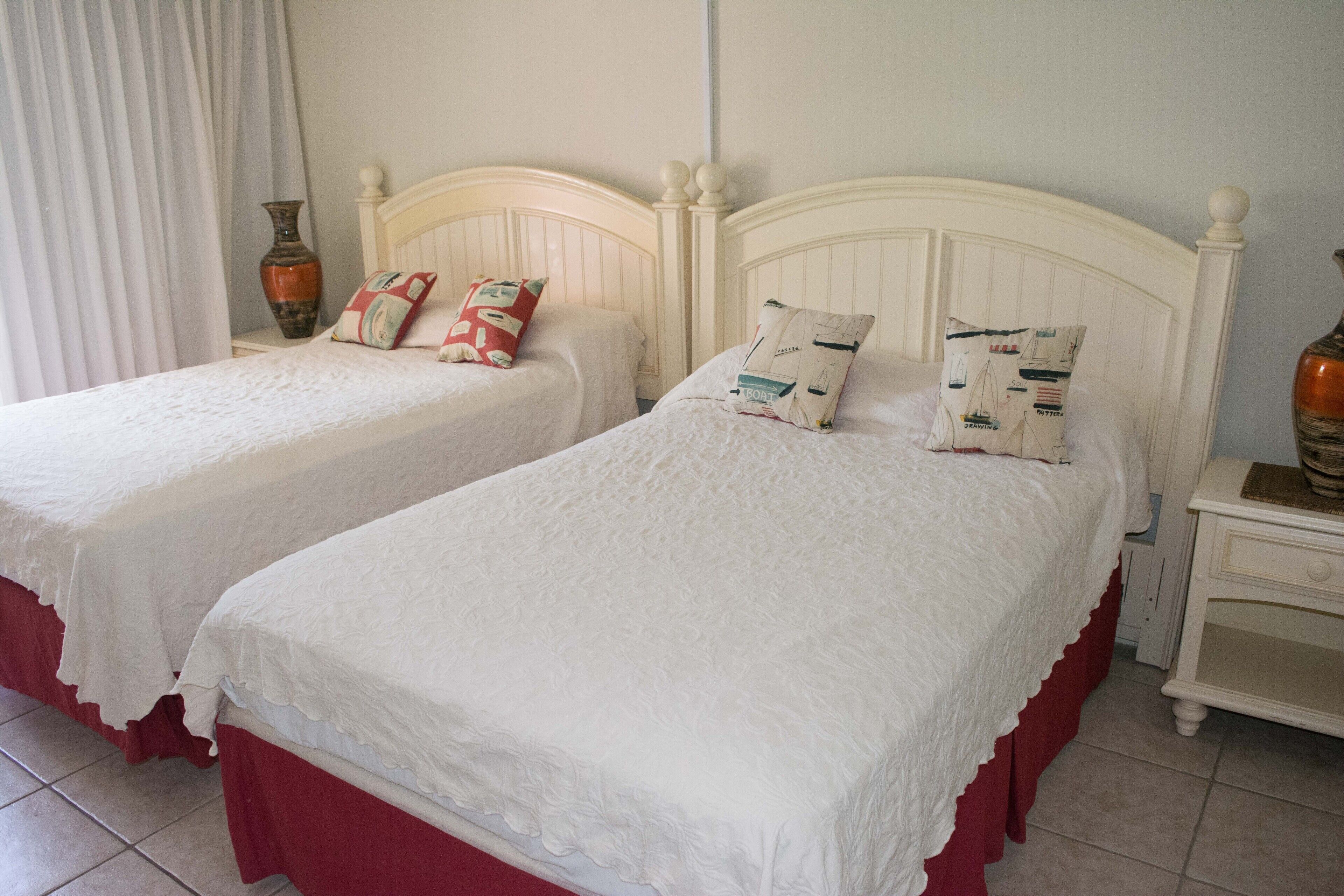 Two single beds with white headboards and red bed skirts, each with decorative pillows and a vase on a nightstand.