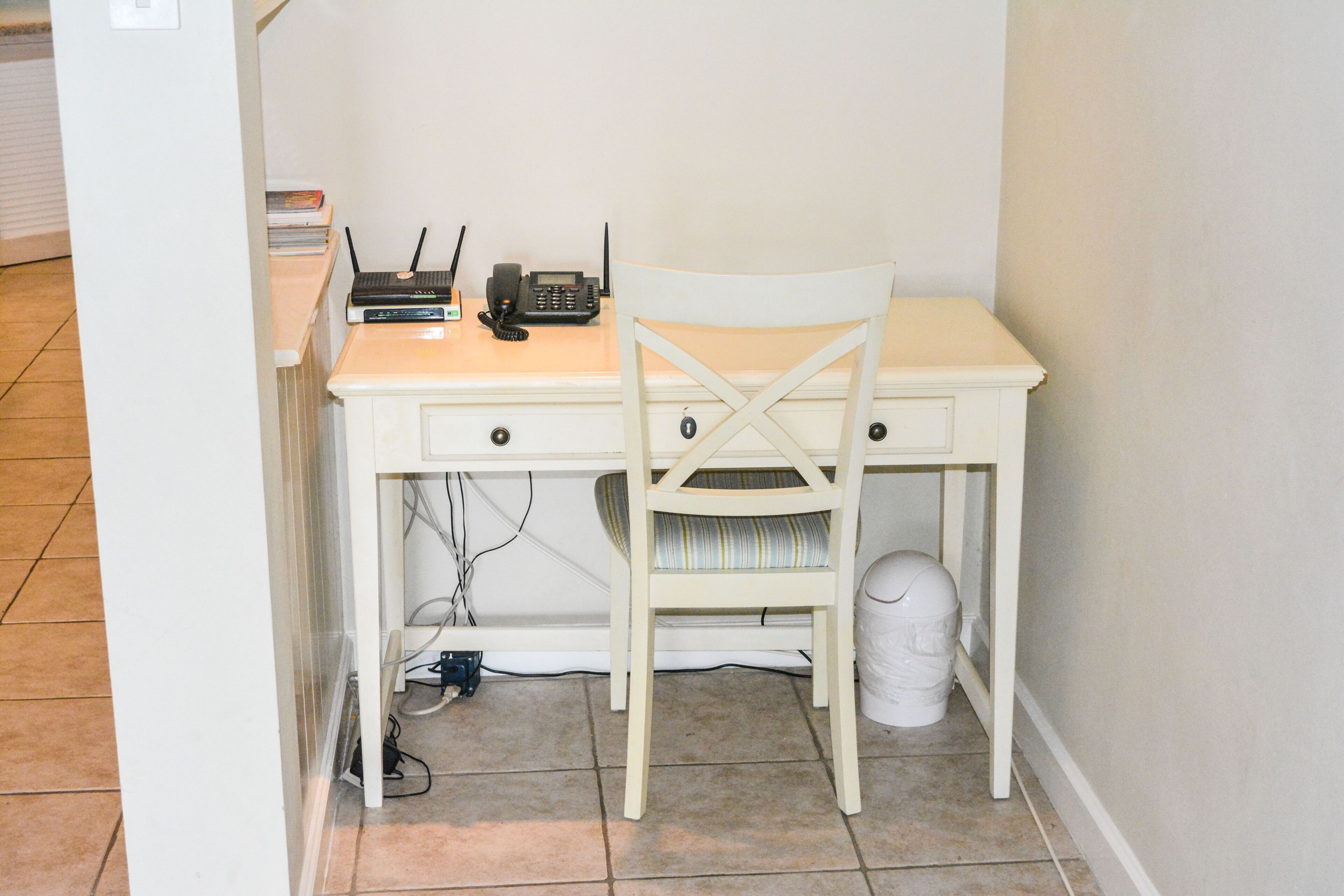 A small, white desk with a chair, a telephone, and a router.