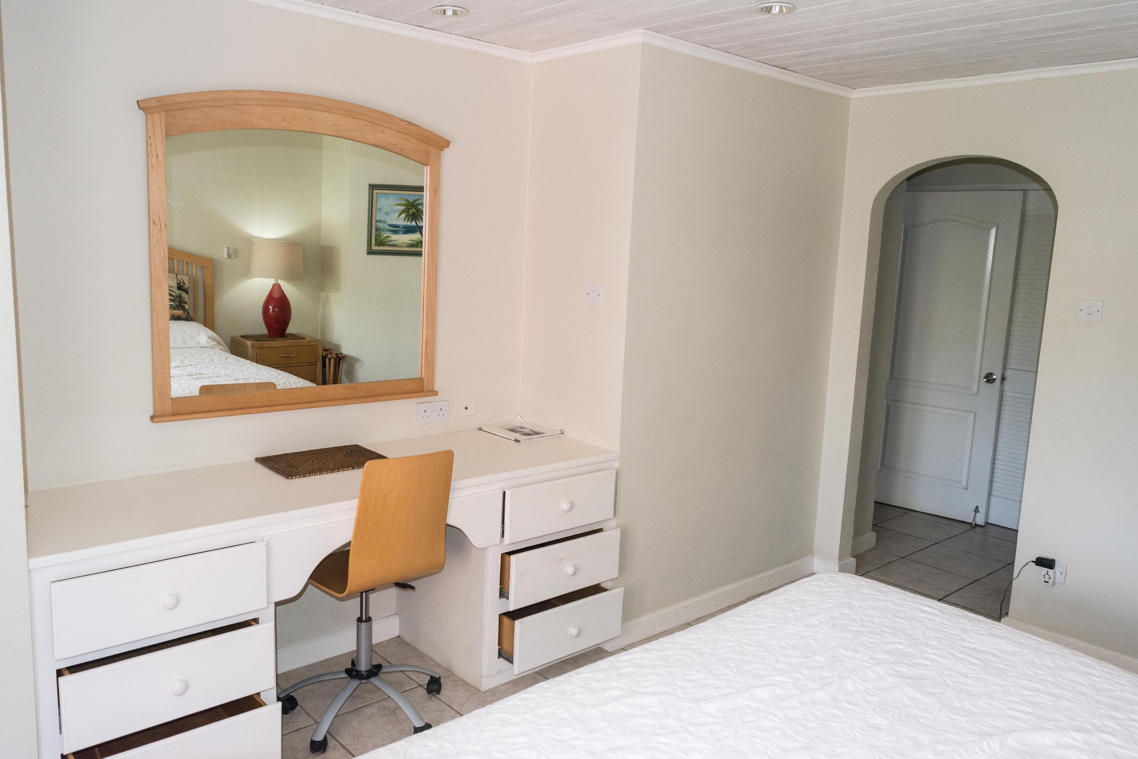 A bedroom with a bed, a desk with a chair, a mirror, and a door.