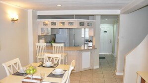 A dining area with a kitchen in the background, featuring a central island, white cabinetry, and a tiled floor. - The Harbour (Gros Islet)