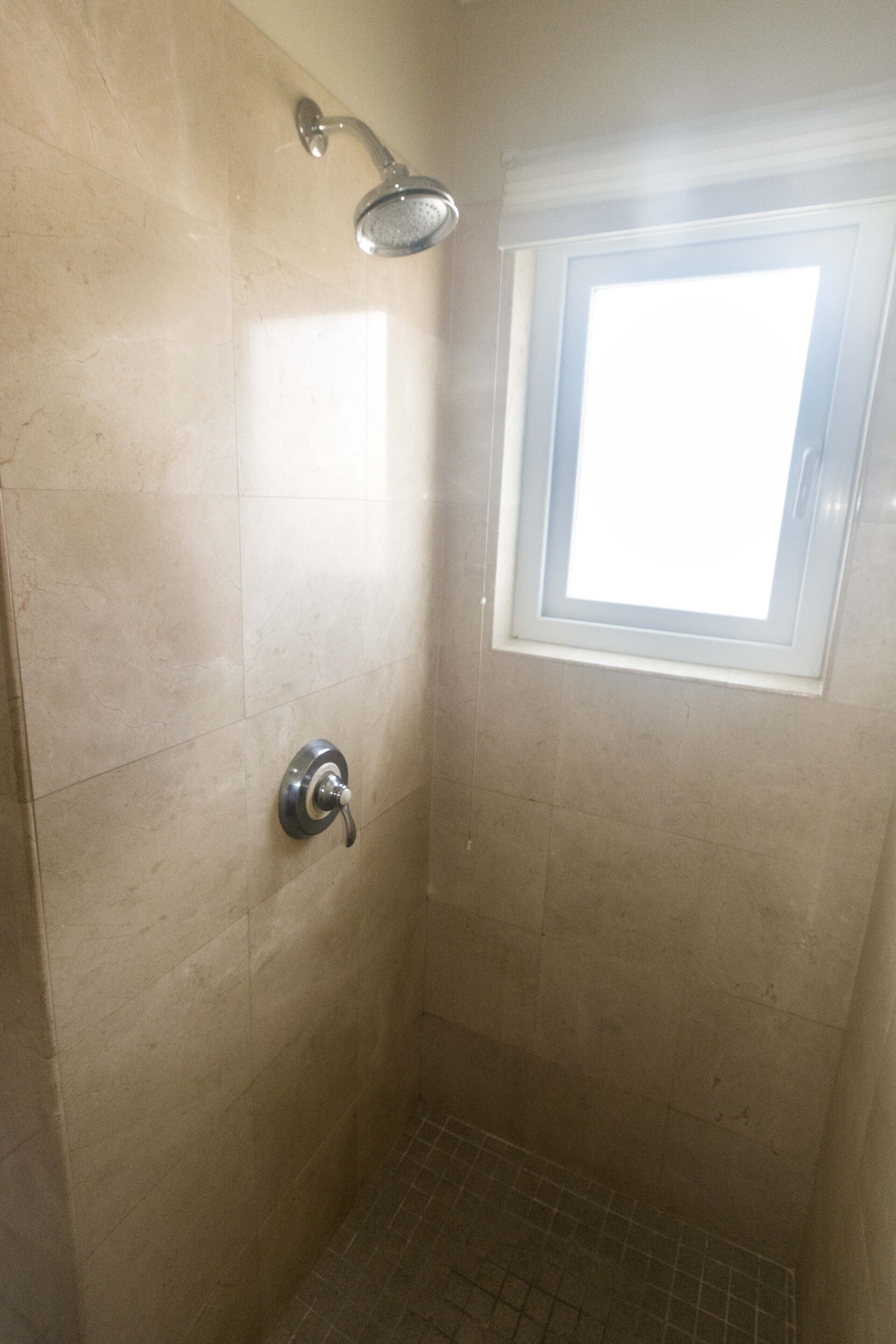 Une petite douche carrelée, dotée d’un pommeau de douche à main et d’une fenêtre située au-dessus.
