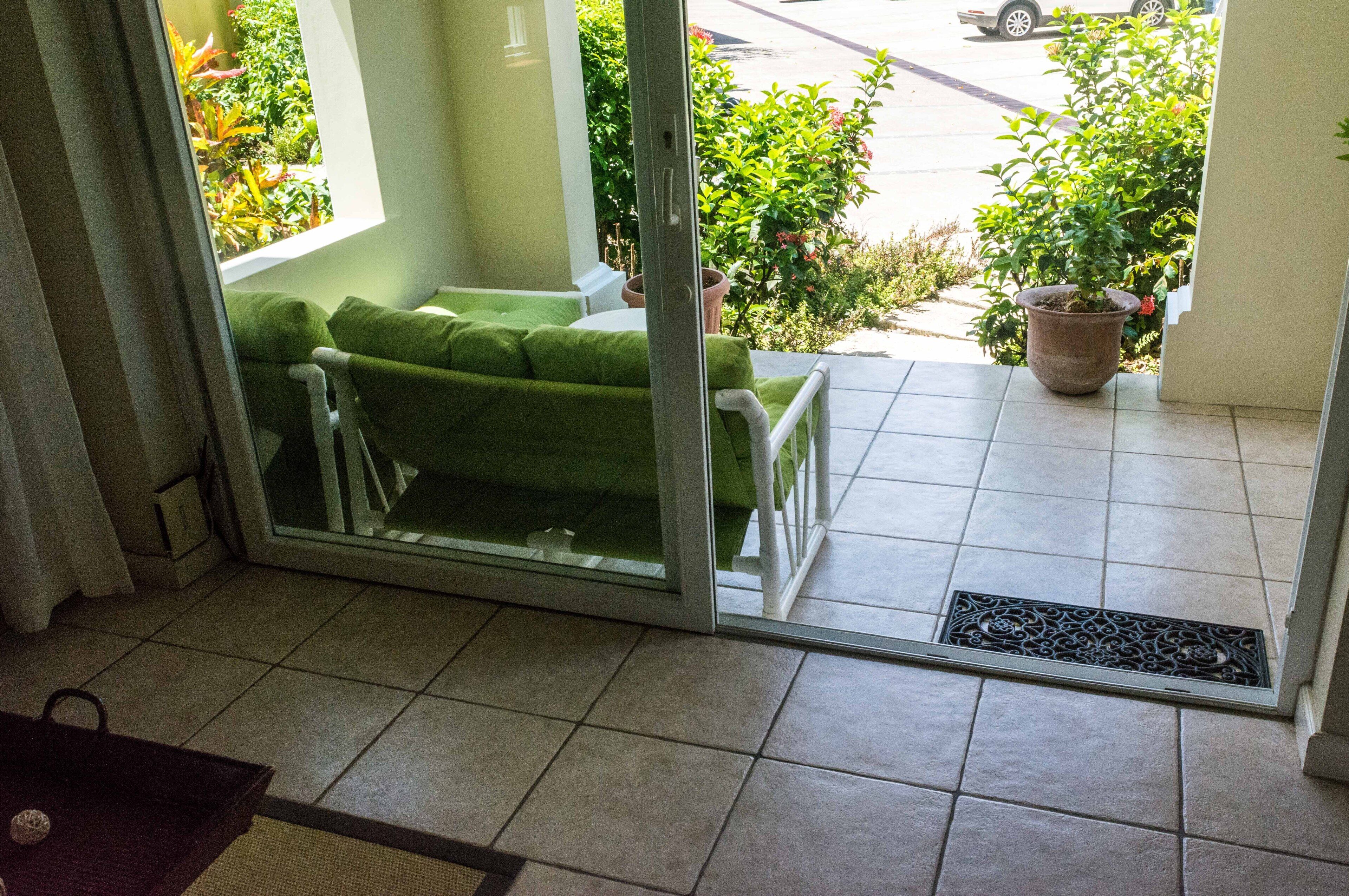 Una habitación con puerta corrediza de vidrio que da a un balcón con sofá verde y plantas en macetas.