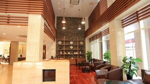 Um hall amplo com balcão de recepção em madeira, área de estar e parede de pedra com relógios.